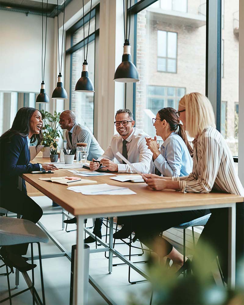 A group of business professionals sitting at a table engaged in discussion. The image represents teamwork and consultation, akin to the Telecom Expense Audit services provided by Chambers Advisory Group to help clients identify cost-saving opportunities.