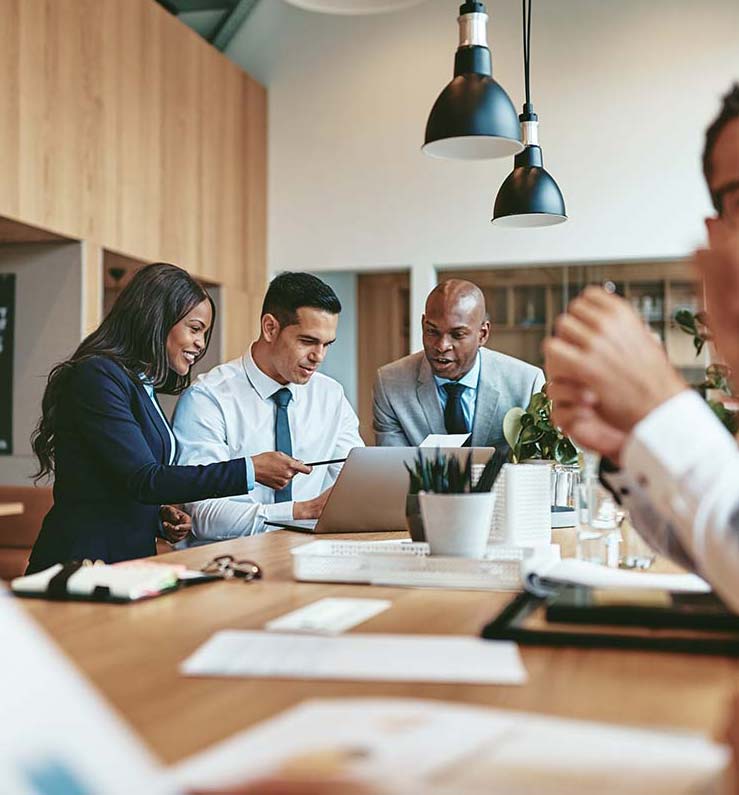 A group of professionals gathered around a laptop, discussing details in a collaborative meeting. The scene represents the teamwork involved in telecom expense management services, as provided by Chambers Advisory Group to help clients achieve cost efficiency.